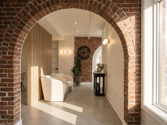 Une arche de brique ouvrant sur un salon aux fauteuils pâles et à la claustra de bois.